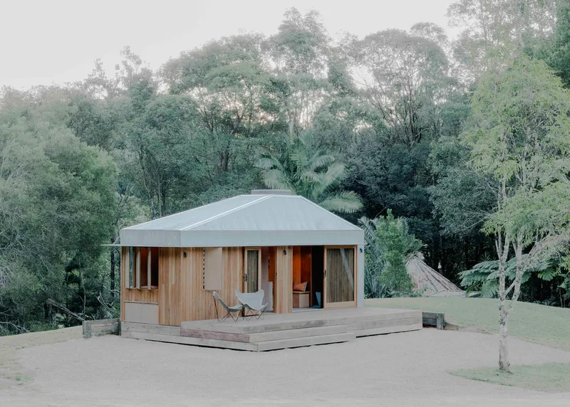 Timber-clad pavilion with corrugated metal roof and timber deck terrace surrounded by dense tree canopy