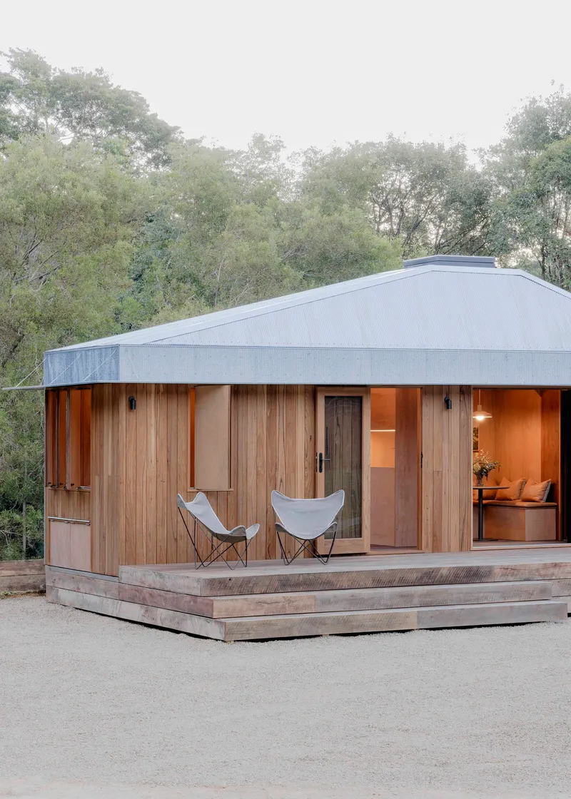 Front elevation showing vertical timber cladding with glazed openings and two canvas chairs on the deck