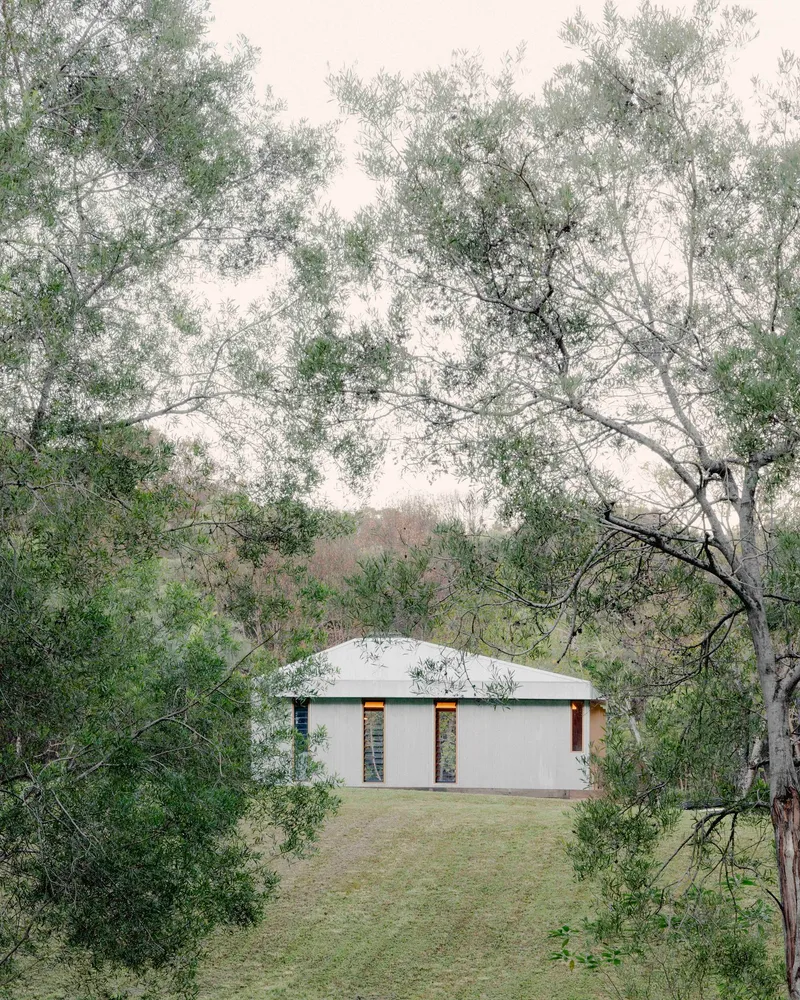 Rear view of the gabled volume in mist with twin openings visible through surrounding eucalyptus trees