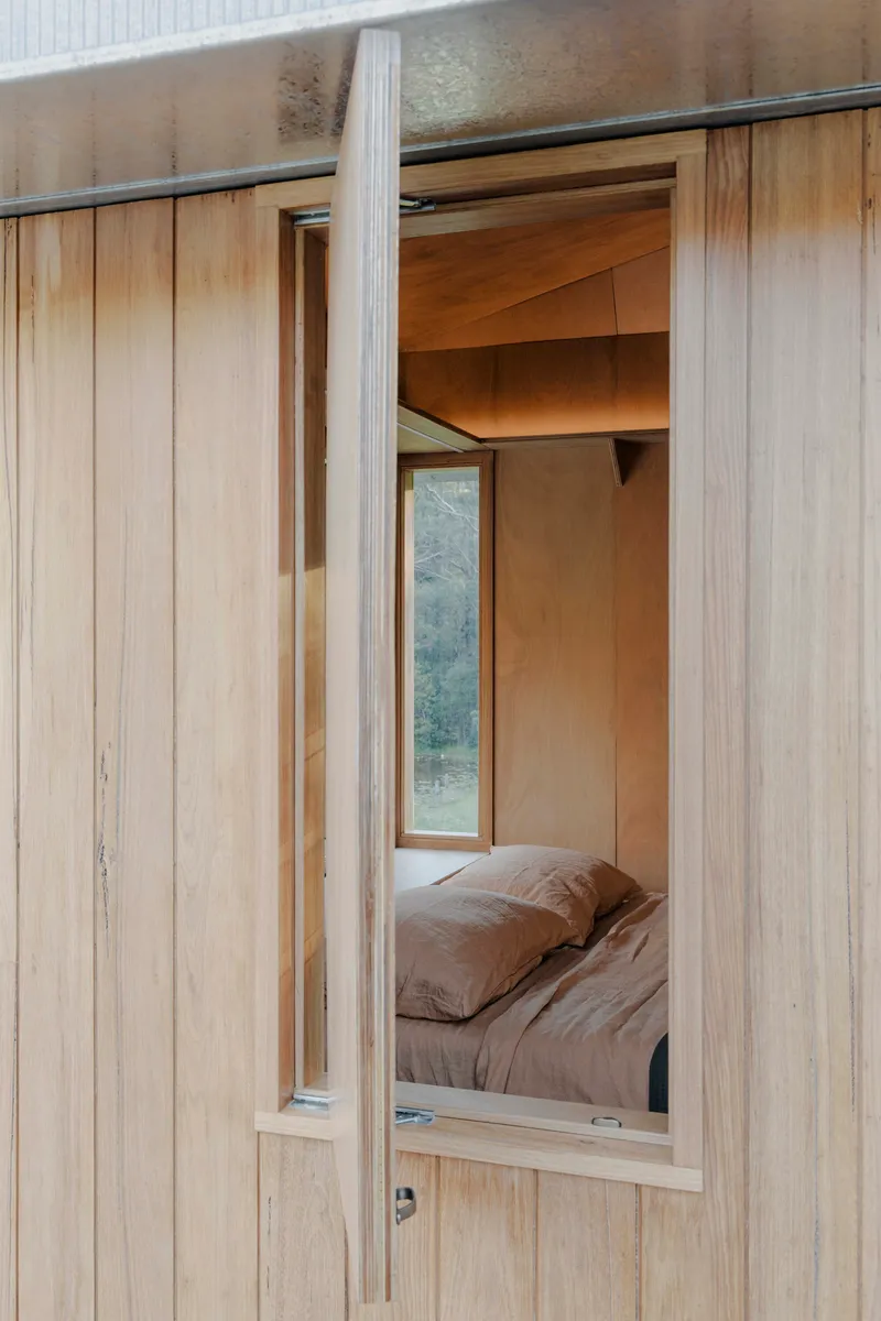 Vertical timber cladding frames the open doorway revealing the plywood-lined bedroom within