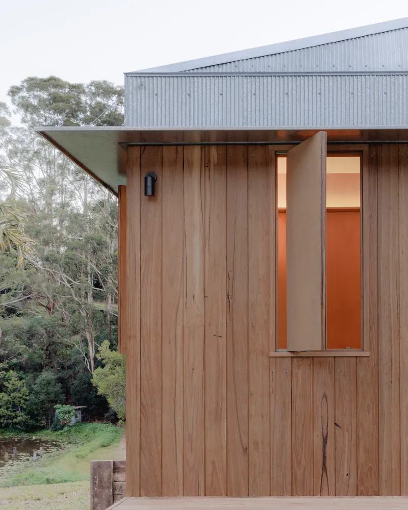 Exterior facade with vertical timber cladding beneath a corrugated metal roof and eucalyptus trees