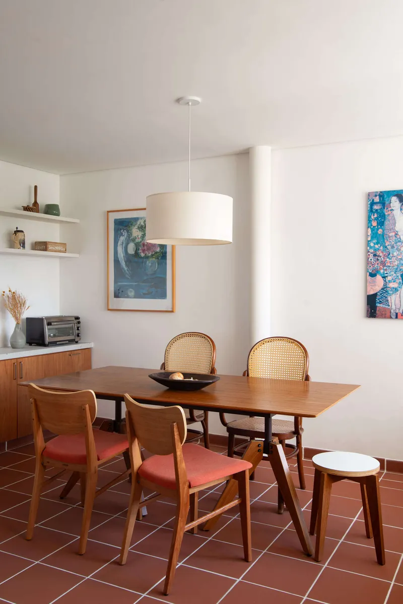 Dining area with wooden table and cane-backed chairs on terracotta tile floor under pendant light