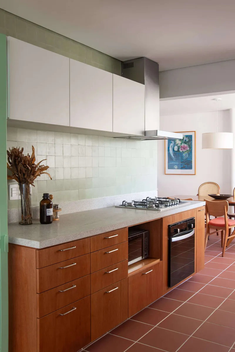 Kitchen counter with terrazzo surface, wood cabinets and pale green tile backsplash under white upper storage