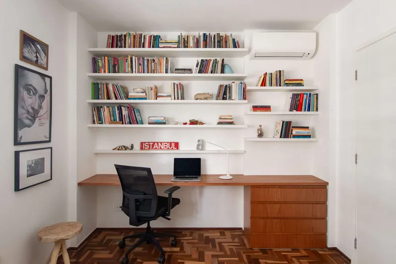 Home office with wall-length wood desk, white floating shelves and herringbone wood flooring