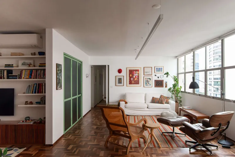 Living room with herringbone wood floor, green-framed sliding doors and floor-to-ceiling windows overlooking the cityscape