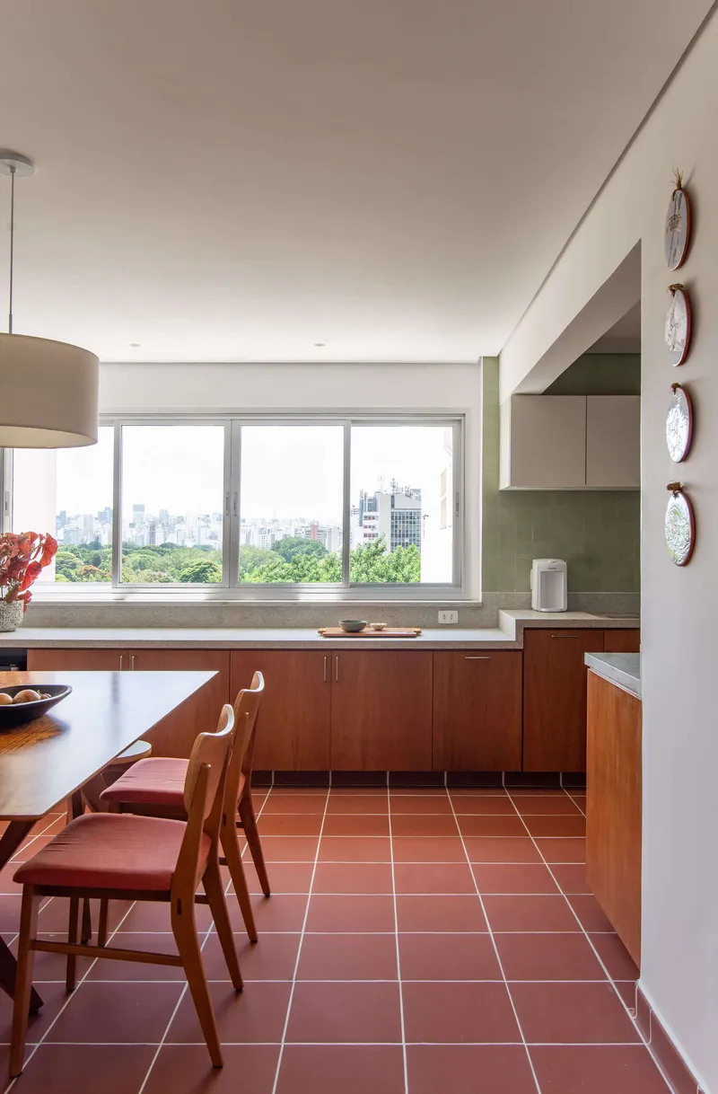 Kitchen with terracotta tile floor, wood cabinetry and a wide window framing treetops and distant towers