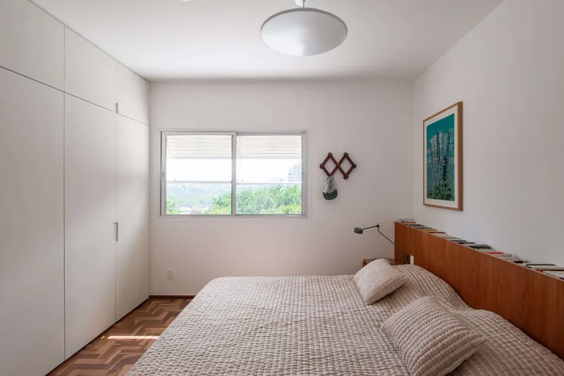 Bedroom with herringbone wood flooring and sliding window framing greenery beyond