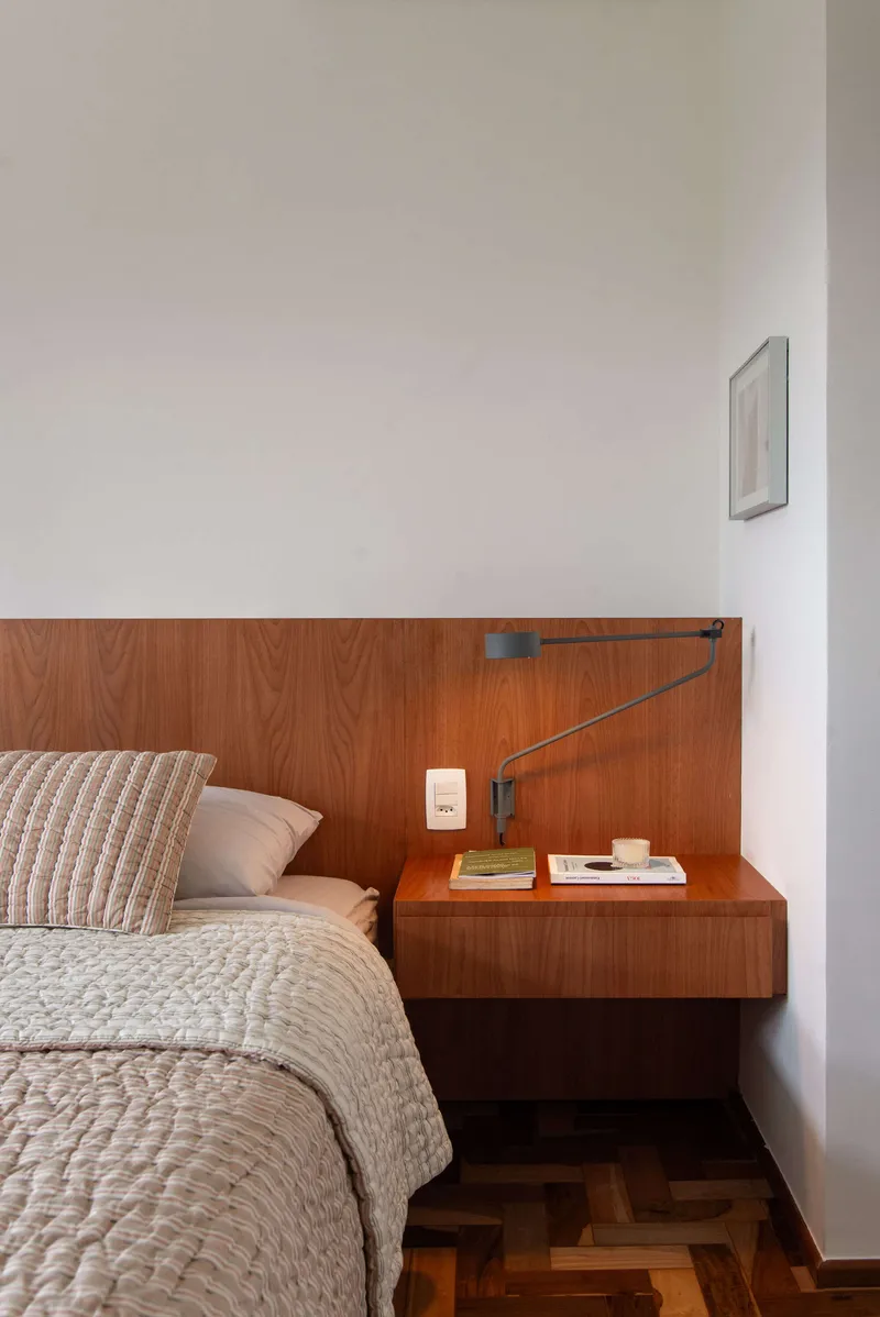 Floating timber nightstand with wall-mounted lamp above herringbone wood floor