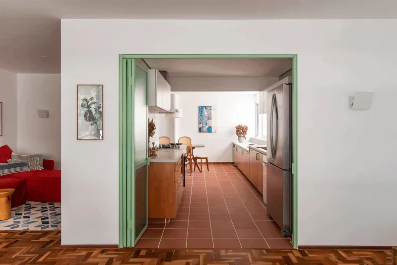 View through mint green folding doors into the kitchen from the living room with herringbone parquet flooring