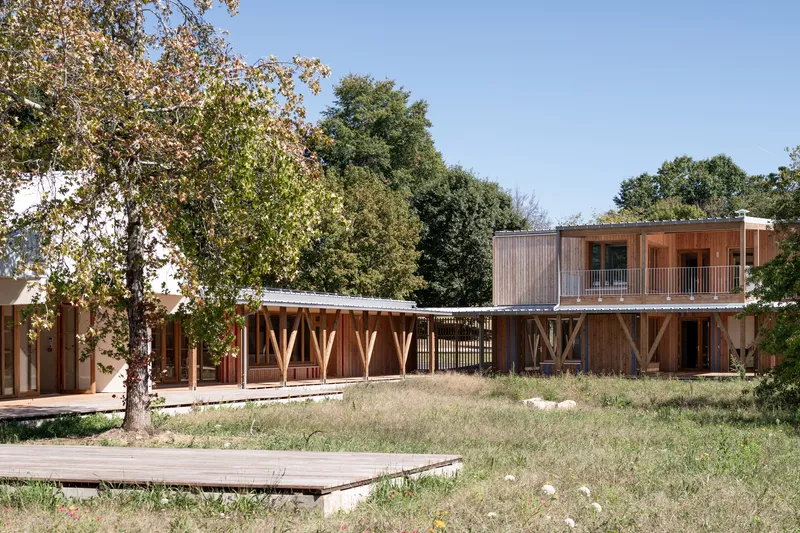Cluster of low-slung timber buildings with metal roofs around a meadow courtyard in summer
