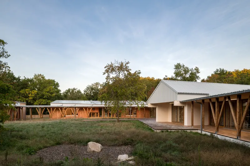 Courtyard view of linked pavilions with timber structure and metal roofing at dusk