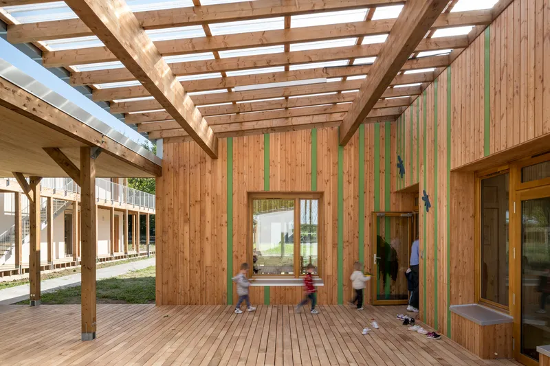 Courtyard view of timber cladding with green vertical stripes and children playing under the pergola