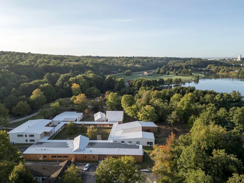 Aerial view of the interconnected white roof volumes nestled among dense forest and lake