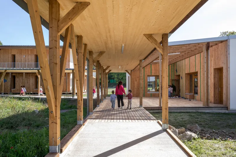 Covered walkway with laminated timber columns and plywood ceiling as a caregiver walks with children