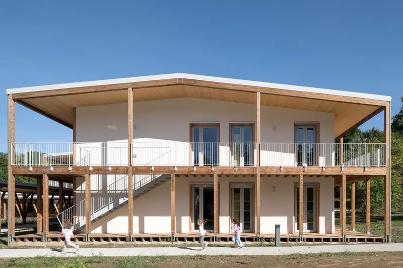 Two-storey timber structure with exposed wooden columns and elevated walkway under a clear blue sky