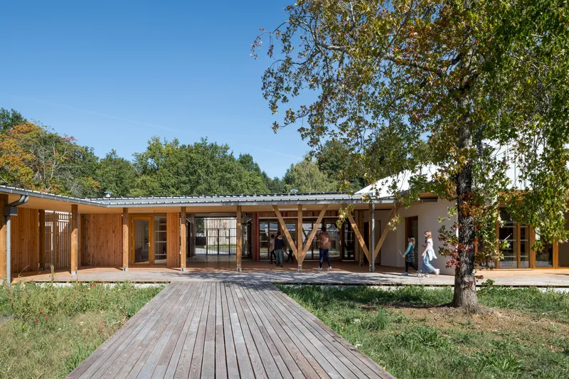 Timber boardwalk leading to covered colonnade with diagonal bracing beneath a mature oak tree