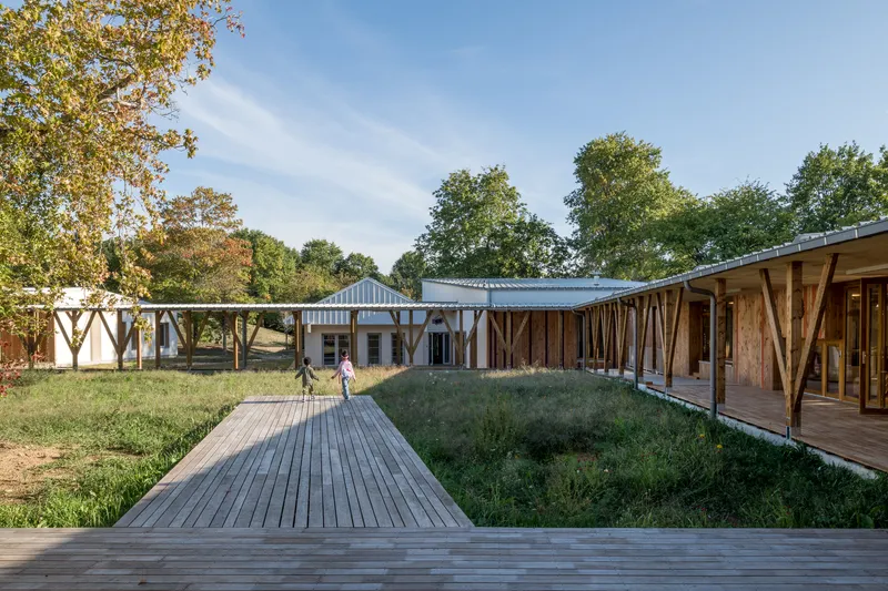 Timber boardwalk connecting volumes arranged around a grassed courtyard with children walking among the buildings