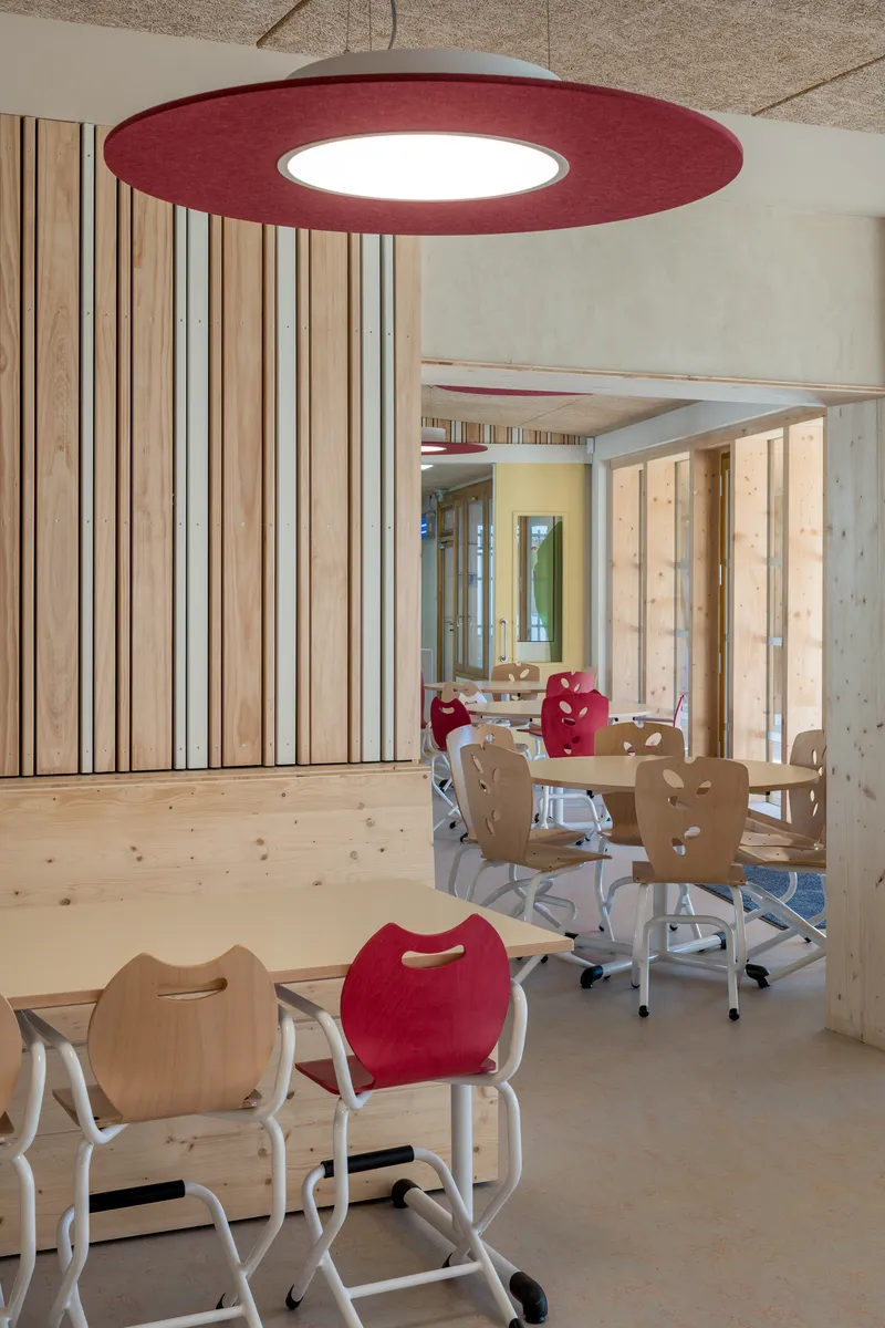 Dining area with maroon disc pendant light and plywood chairs arranged at low tables