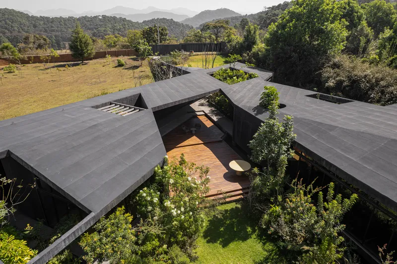 Drone view of clustered gabled roofs forming courtyards with planted beds and timber walkways linking the pavilions