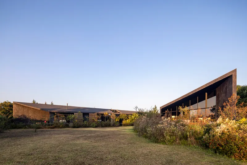 Low-pitched roof pavilions with timber and stone facades separated by open lawn and garden at dusk