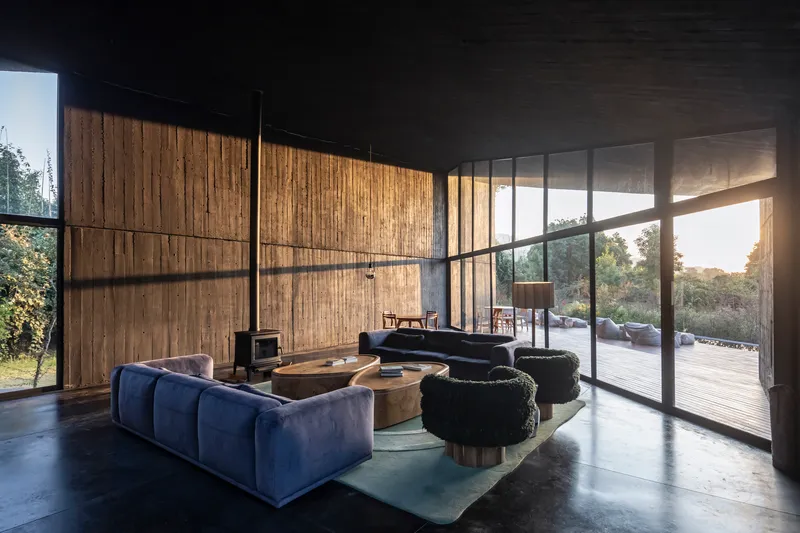 Interior living space with vertical timber wall panels and floor-to-ceiling glazing opening to timber deck at sunset