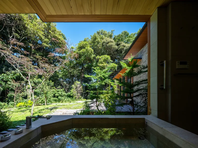 Concrete soaking tub on covered terrace opening to lawn and forest in bright daylight