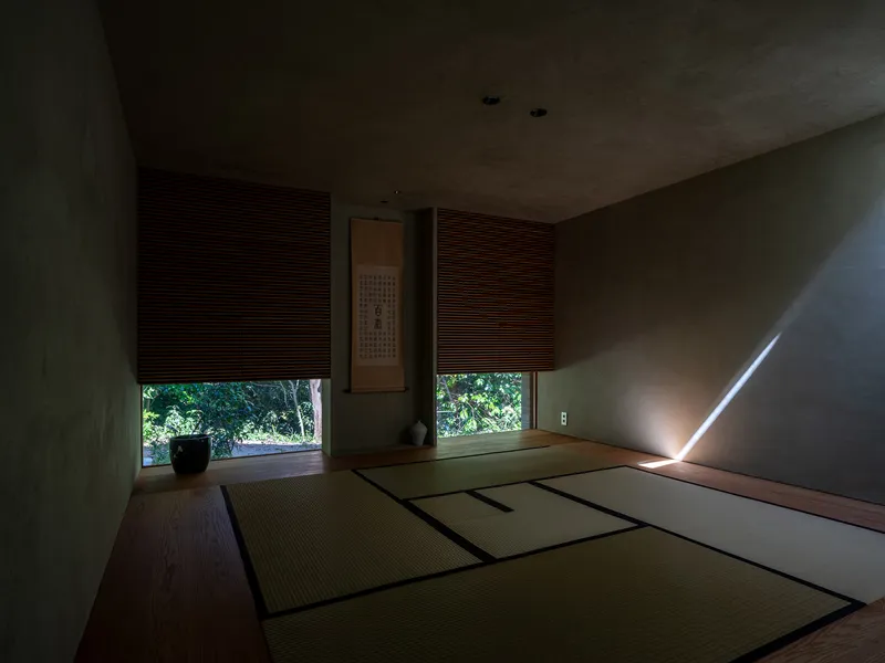Tatami room with lowered bamboo shades and thin shaft of daylight across the floor