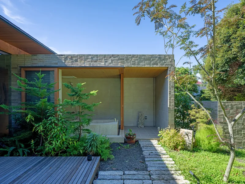 Covered outdoor bathing area with concrete block wall and timber ceiling overlooking garden with stepping stones