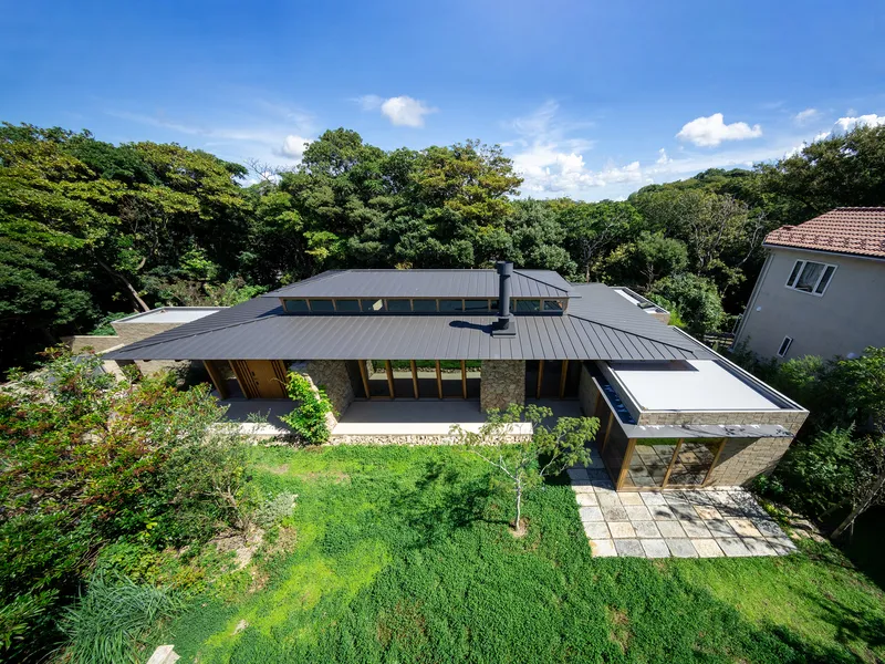 Aerial view of the low-slung metal roof volumes surrounded by lawn and forest canopy