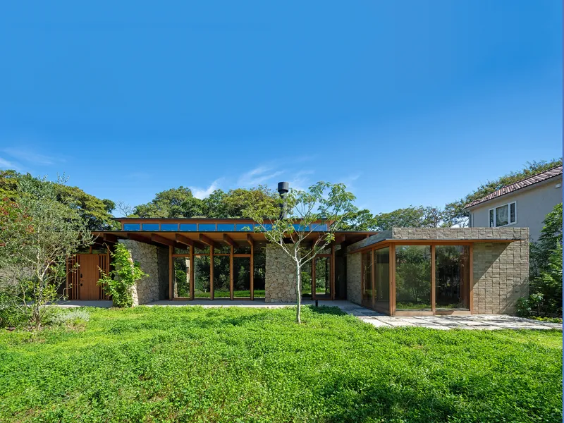 Garden elevation showing stone walls and timber-framed glazing under a flat roof on a sunny day