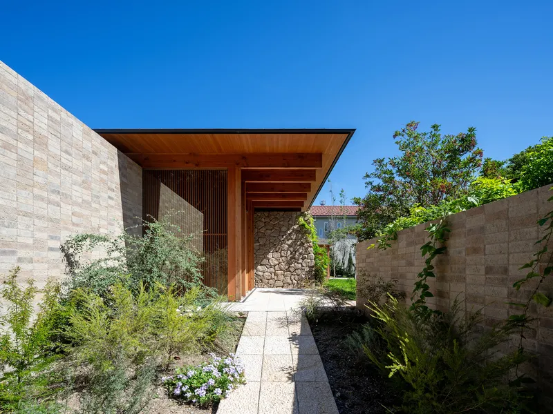 Entry courtyard with planted beds between stone block walls leading to a timber-clad entry portal