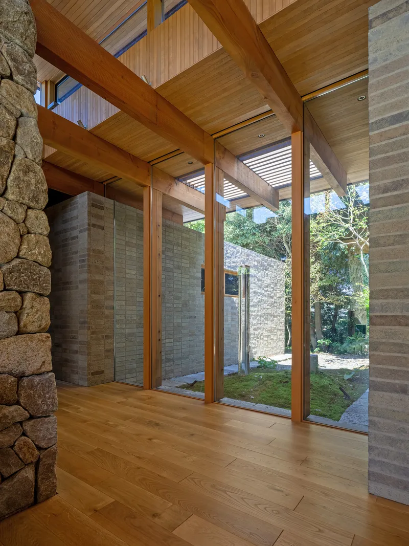 Floor-to-ceiling glazing between timber posts with fieldstone wall and courtyard beyond