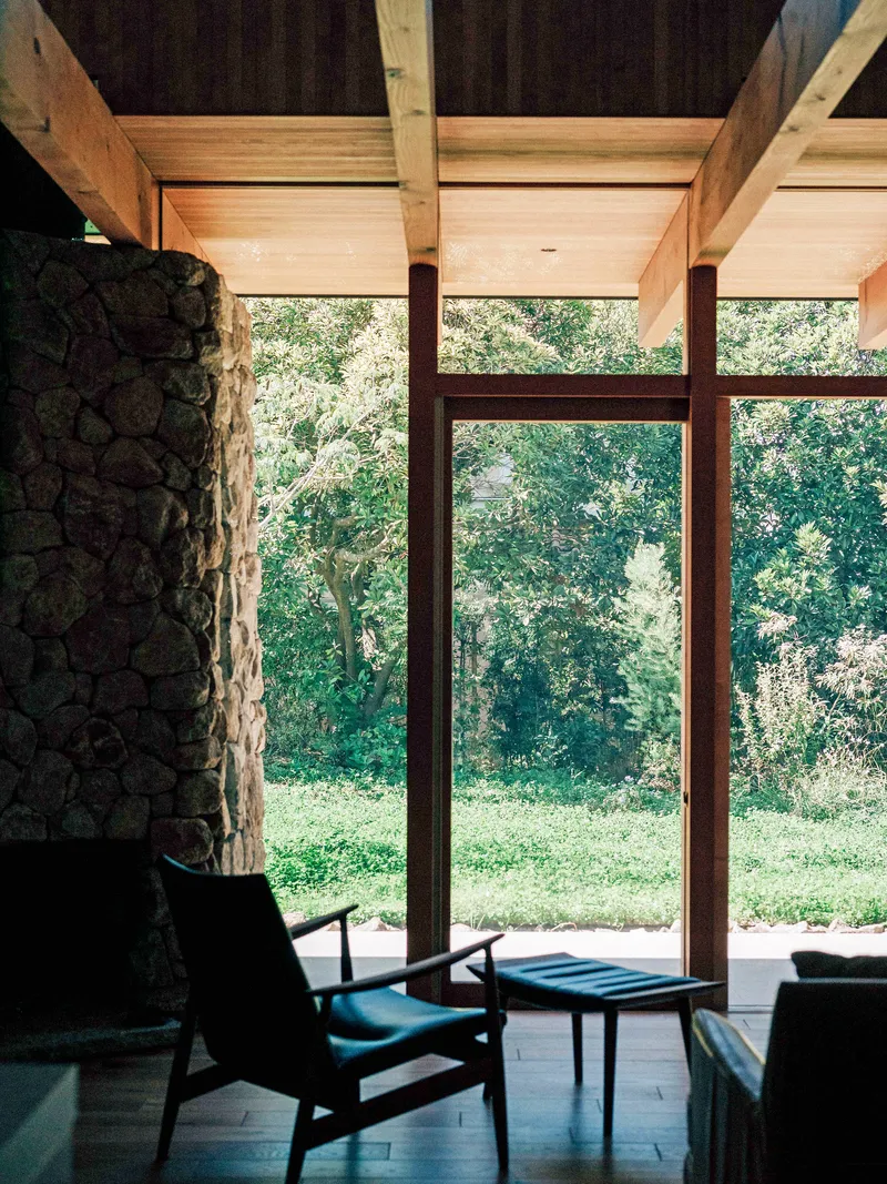 Interior living area with exposed timber beams and stone wall framing glazed doors to the garden