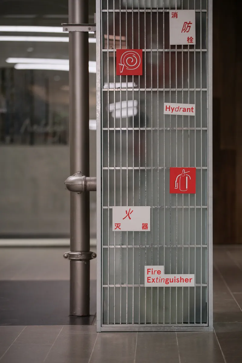 Metal mesh fire safety cabinet with red and white bilingual signage beside stainless steel conduit