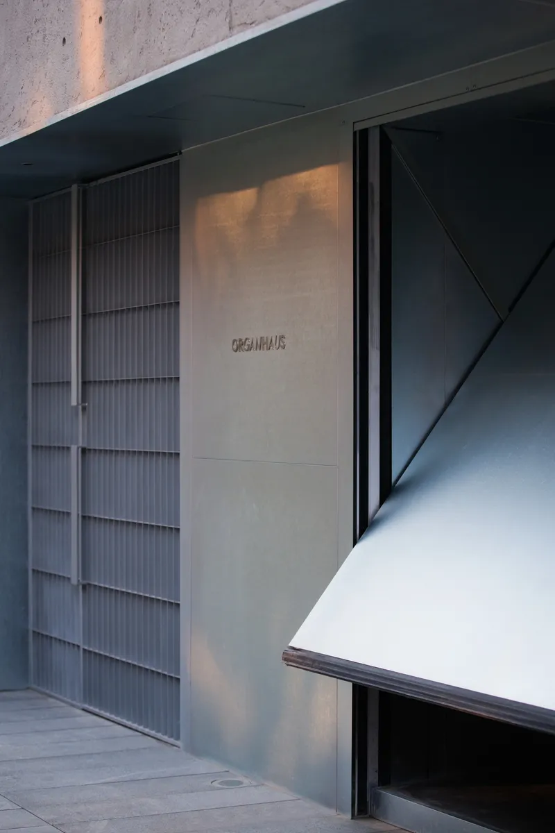 Concrete wall panel with engraved lettering between fluted metal cladding and dark angular ceiling at dusk