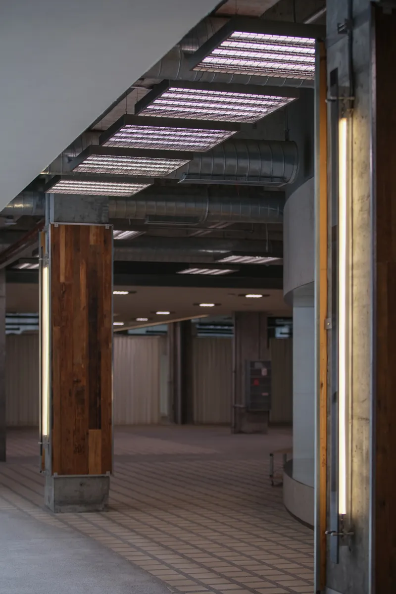 Interior hallway with timber-clad columns featuring integrated strip lighting beneath exposed ductwork and linear ceiling fixtures