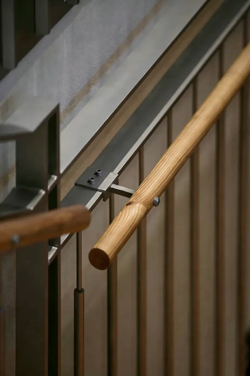 Timber handrail with steel bracket connecting to vertical slat balustrade beside a white ceiling plane