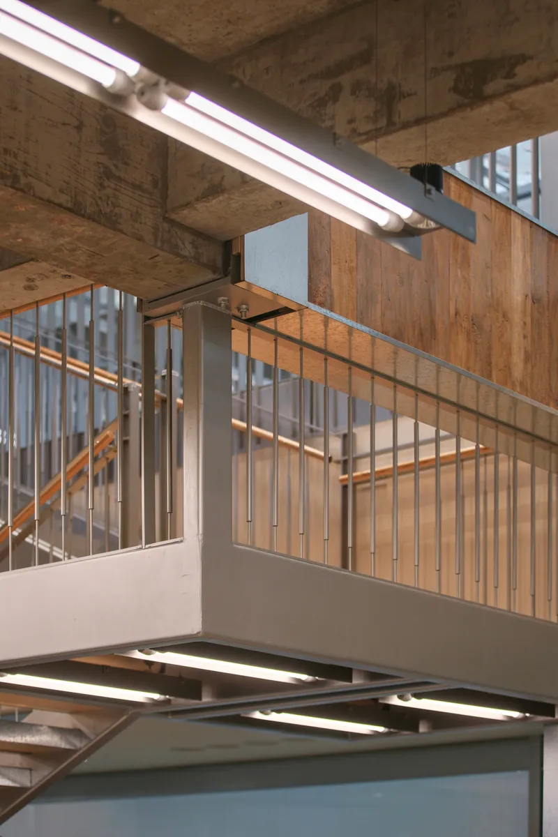 Stairwell with timber slat balustrades and exposed concrete ceiling beams with fluorescent tube lighting