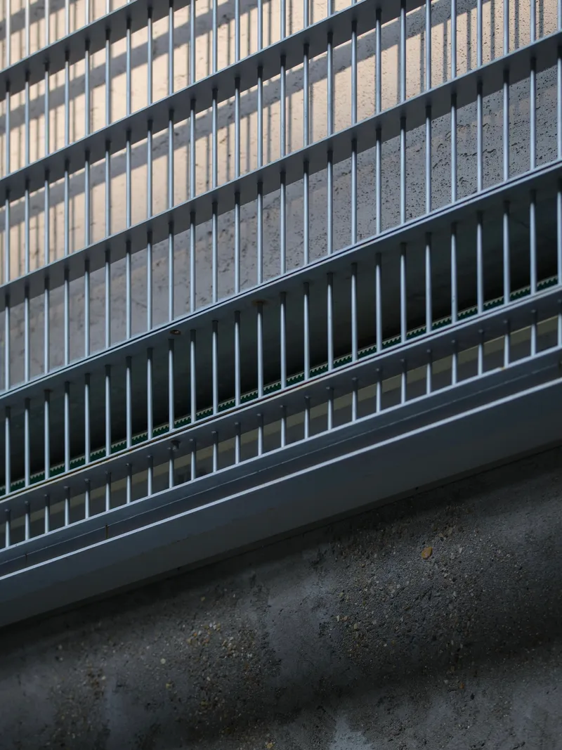 Detail of metal balustrade with vertical fins and horizontal rails meeting a concrete floor