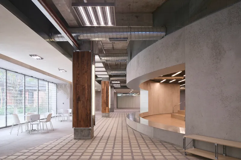 Interior hallway with timber-wrapped columns, exposed concrete ceiling, curved reception desk, and gridded floor tiles