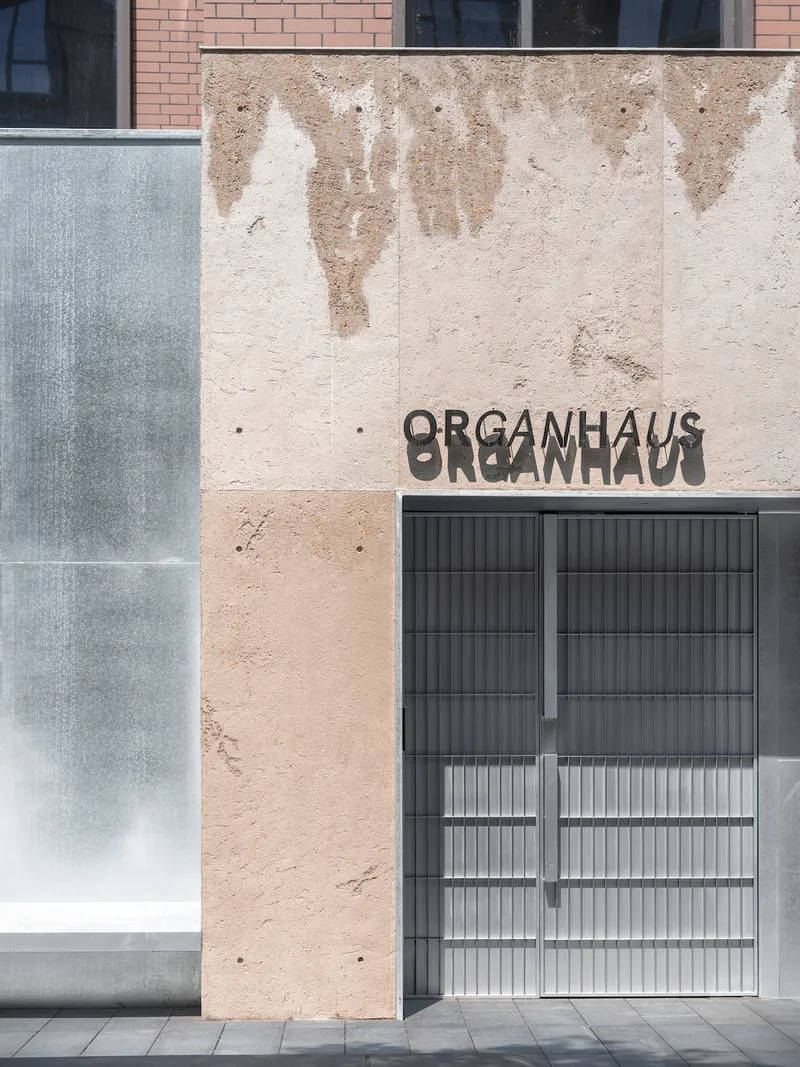 Weathered rammed earth facade with textured layering and metal screen window opening below signage