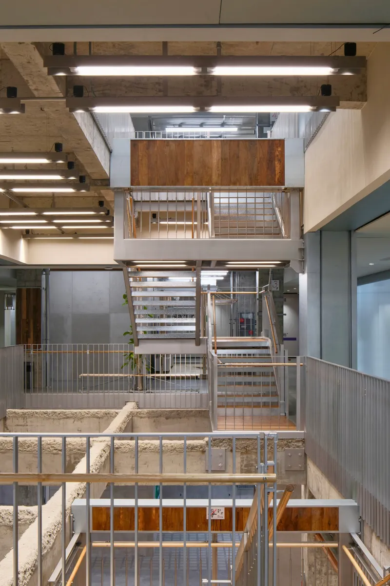 Central atrium looking down through multiple levels of steel stairs with concrete beams and timber panels