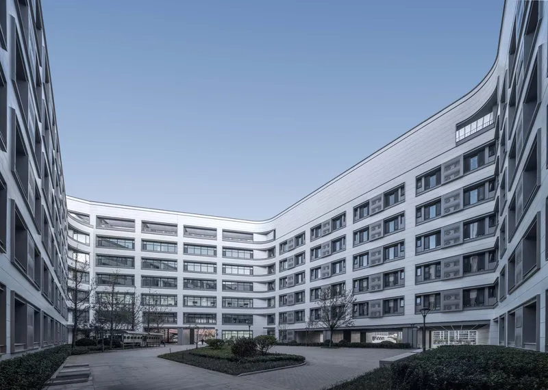 Interior courtyard enclosed by curved white facades with planted beds and bare trees under grey sky