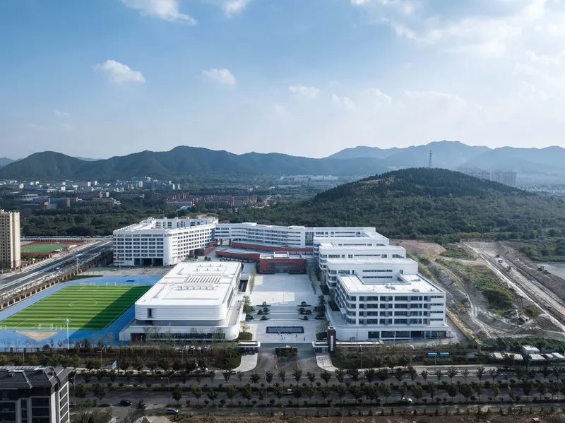 Aerial view of the white campus with athletic fields and terraced courtyards backed by forested hills