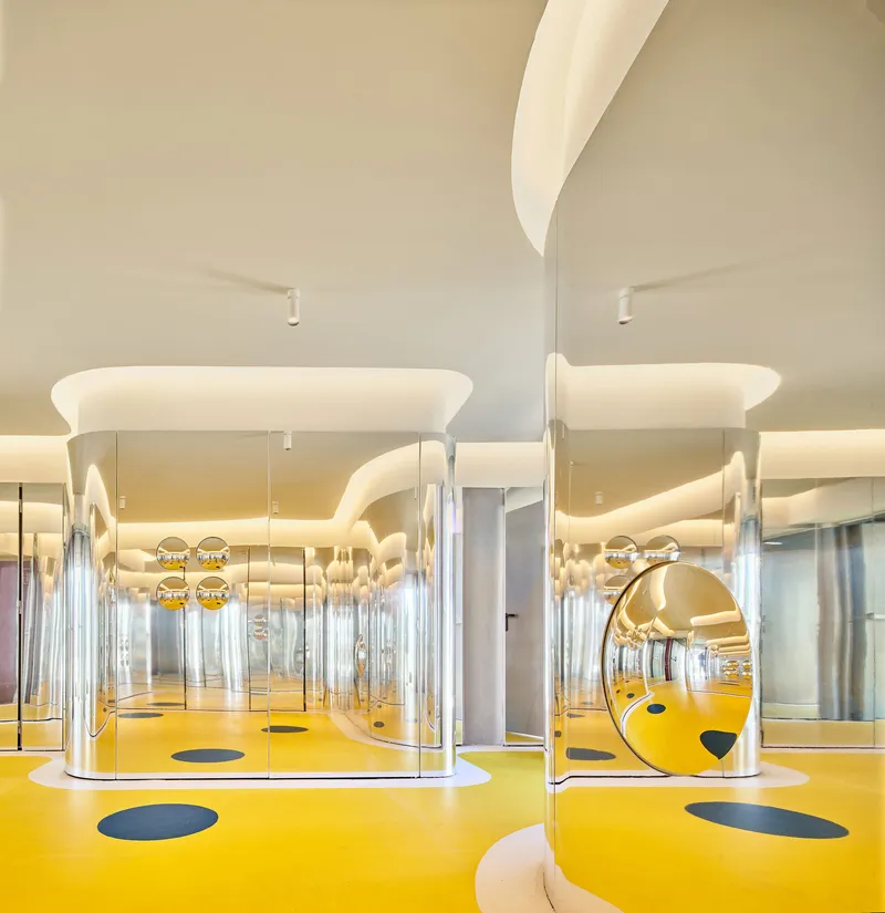 Interior with yellow resin floor and mirrored glass enclosures under sculptural white ceiling panels
