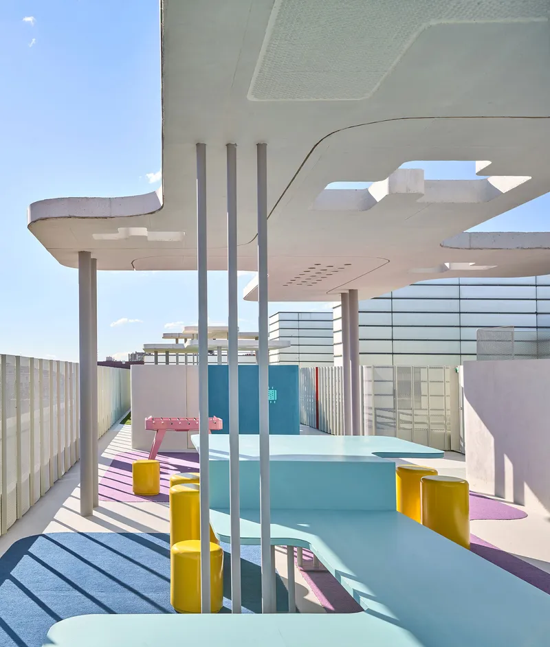 View through cylindrical columns toward pool area with pink decking and mesh screens in bright sun