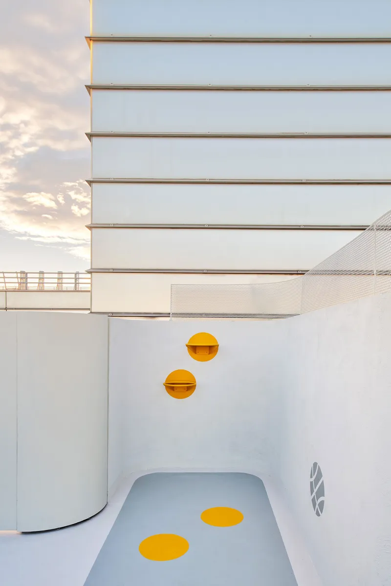 White play slide with yellow circular accents beside horizontal metal cladding at dusk