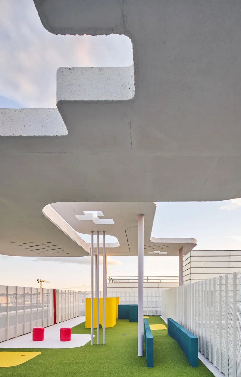 Underside of concrete canopy with perforations and cylindrical supports over artificial turf play area