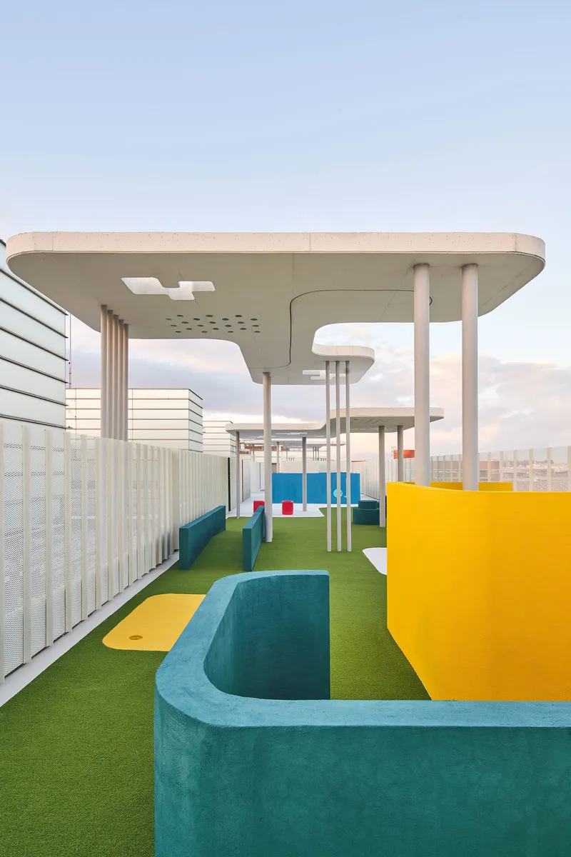 Rooftop play zone with teal and yellow curved seating elements on green turf under cloudy sky