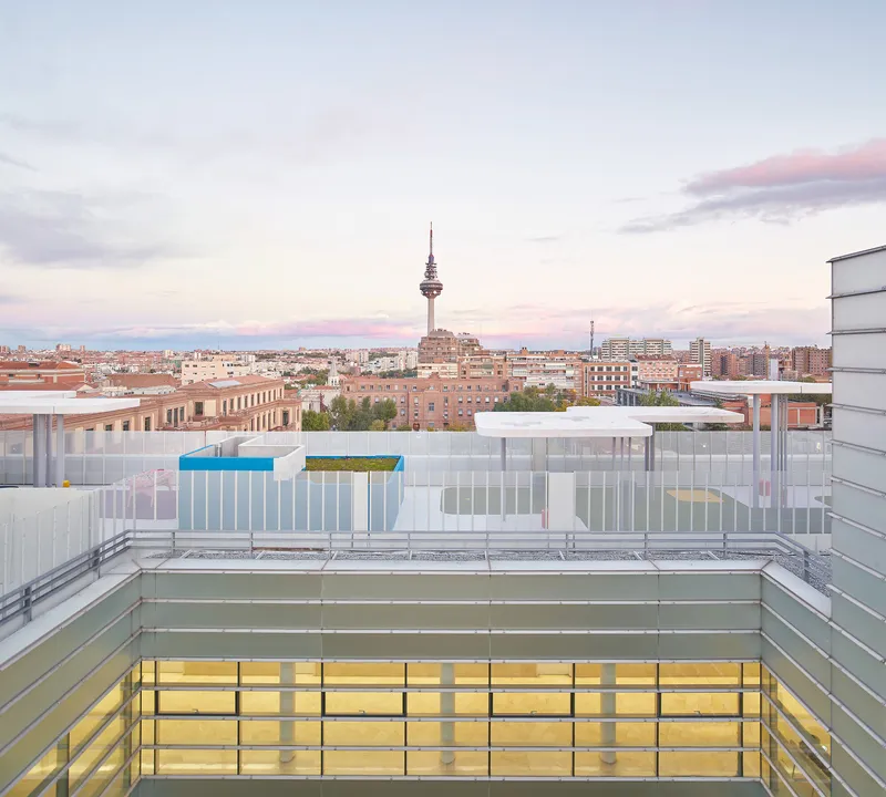 Rooftop courtyard with translucent glass panels and colorful accents overlooking the urban skyline at dusk